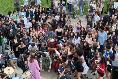 From above, a crowd of a teenage students gathers in front of a band playing on an outdoor stage.