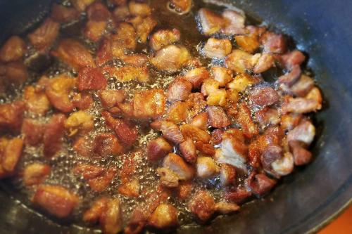 Wok full of browning pork pieces and bubbling oil.