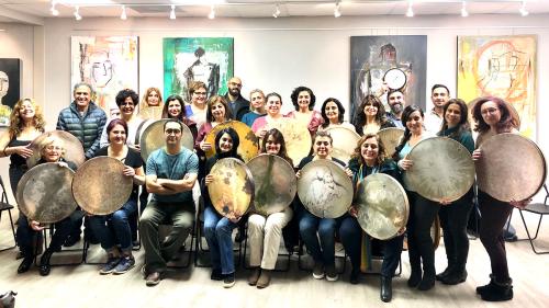 Group pose of 25 people, almost all holding a large, circular frame drum.