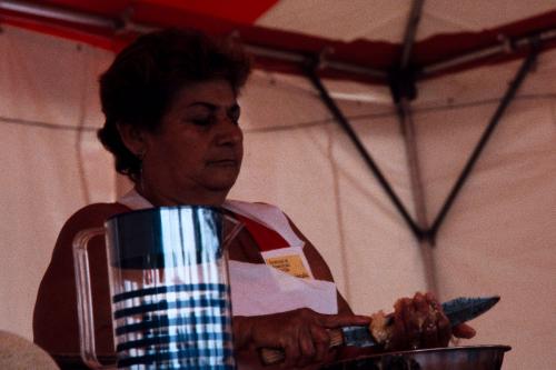 Inside a white and red tent, a woman slices something in her hand with a kitchen knife.