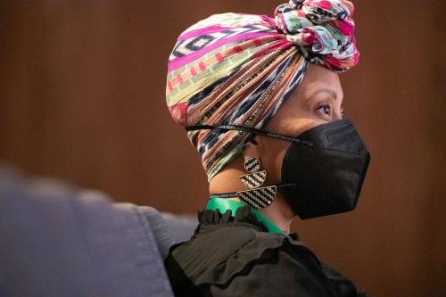 A woman in multicolored patterned headwrap and black face mask looks up toward the stage.