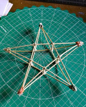A three-dimensional star made out of small wooden sticks sits on top of a green cutting board.