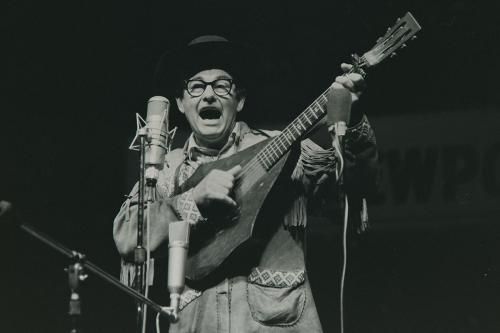 A man plays guitar on stage, his mouth wide agape as  he sings.