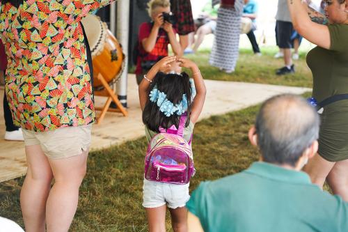 A young girl wearing a blue lei on her head puts her arms up over her head while dancing.