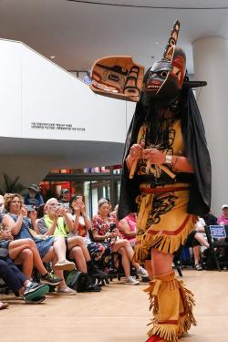 A performer controls their articulated wooden mask with handles attached to strings; one face opens vertically to reveal a different face inside.
