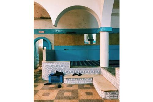 A Turkish bath room with white, arched ceilings, walls that are blue, white, and beige, and tiled floors of the same color palette. 