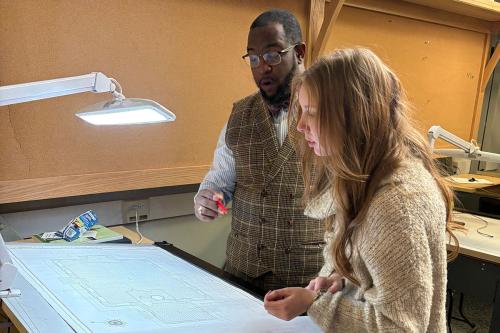 Two young people inspect something out of frame. One holds a pen and looks surprised.