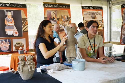 A woman forms one of four spouts on a light brown clay jug shape.