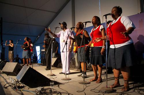 The Jones Family Singers, dressed in red and purple, sing with their arms extended on stage.