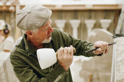 A man uses a mallet and a chisel to carve a large block of white stone.