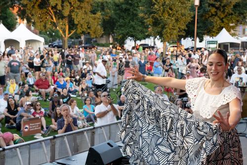 A woman in top white and black and flowing white patterned skirt dances on stage in front of a crowd of people.