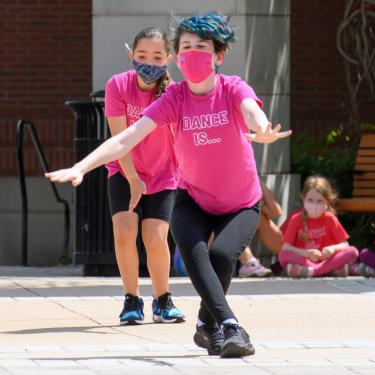 Two dancers in matching pink shirts performing on asphalt outdoors.
