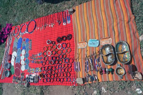 Beaded necklaces, bracelets, and other adornments arranged on red and orange woven textiles on the ground.