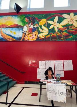 The mural hangs in a hallway with bright red walls, above a staircase and an information table.