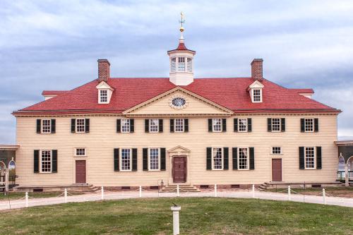 Exterior of a two-story yellow building with red tiled roof, green window shutters, and a central tower.
