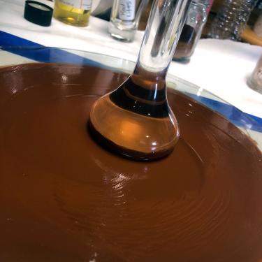 On a circular glass plate, a smooth, brown, oily substance is ground with a clear glass pestle.