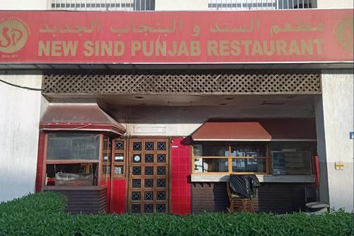A restaurant exterior, with boxy, green shrubbery outside. The facade of the restaurant is red and gold. The sign is in English and in Arabic. 