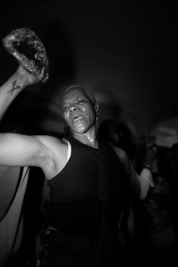 A person, covered in sweat, dances with a tambourine in one hand.