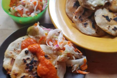 Three dishes: finished pupusas piled up, curtido slaw, and a full serving with pupusas, curtido, and red sauce.