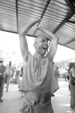 A person dances and shouts, mouth wide open and arms raised to expose a bare belly.