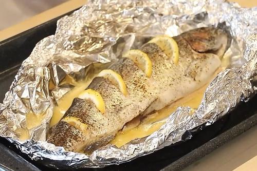 Whole cooked fish in pale liquid, in tinfoil, with lemon wedges placed into its skin.