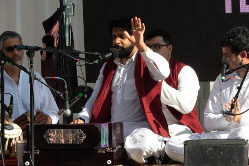 Riyaaz Qawwali, in white shirts and red vests, sing seated on the stage.