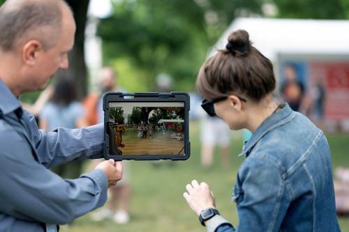 Two people look at a tablet screen, showing an augmented-reality view of the National Mall, with a digital camel sitting to the side.
