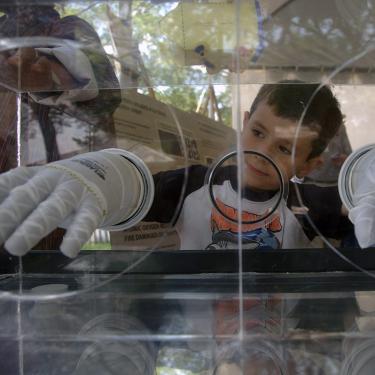 A young boy sticks his hands into two white gloves within a clear box.