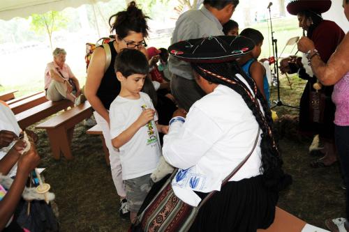 Seated artists show children and adults their weaving tools.