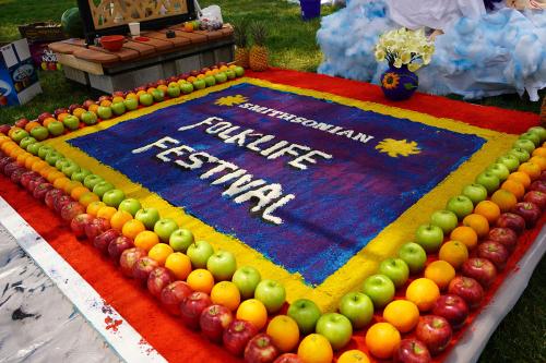 The alfombra’s first scene, which features the Smithsonian sunbursts and the Festival logo, adorned with apples, orange, pineapples and flowers at the feet of the Altar.