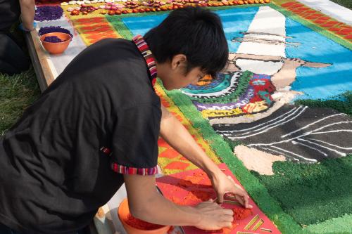 Kevin Cabrera Sánchez at work on the alfombra, using a stencil to place the outline of the Maya woman weaving scene.