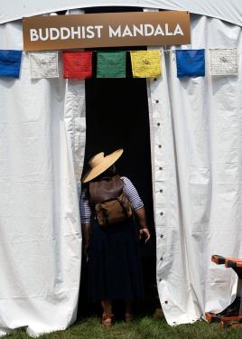 A person peers into a white tent, dark inside, with Tibetan prayer flags and a sign that reads BUDDHIST MANDALA.