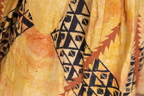 Close-up on a piece of fabric dyed yellow-orange with geometric patterns in black and brown..
