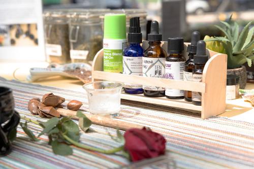 Close-up on small glass tincture bottles in a wooden display shelf and a drying red rose on a table.
