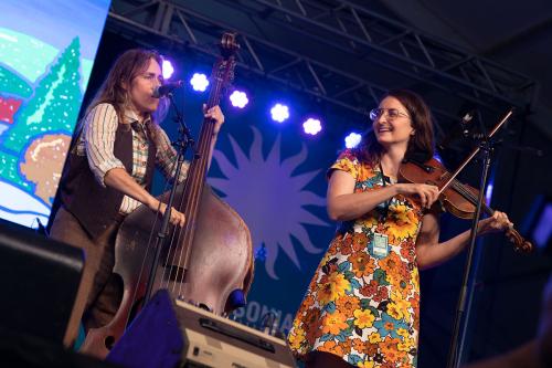 Two women perform on stage, playing upright bass and fiddle.