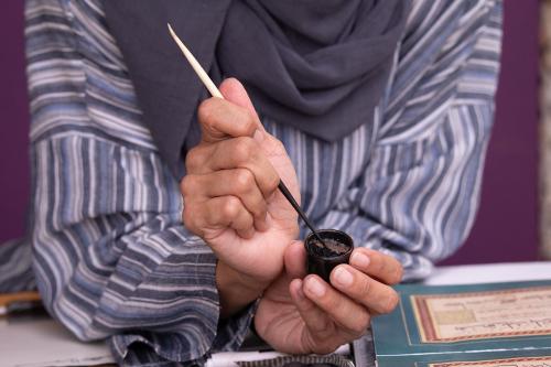 Close-up as a woman dips the tip of a stylus into a small pot of ink.