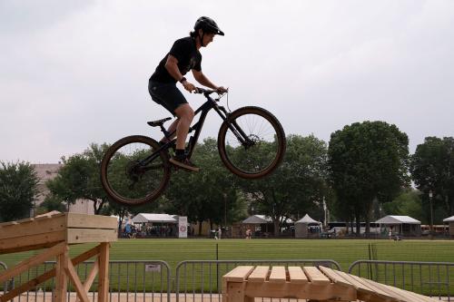 A person on a mountain bike in mid-air, between two sections of a wooden boardwalk.