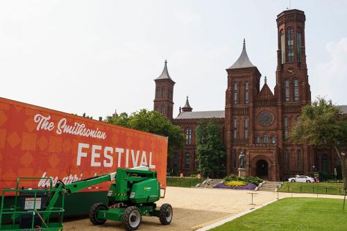 An orange trailer with the words “The Smithsonian Folklife Festival has arrived” spray painted on is parked on the National Mall, with the red Smithsonian castle behind. 