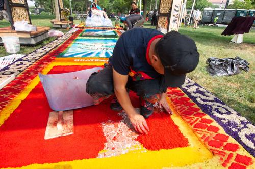 Ubaldo Sanchez kneels down, working on the last scene of the first alfombra, the day after one of the first storms of the Festival in which the alfombra got flooded.