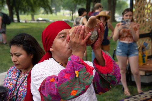 Close up of Ubaldo Sanchez blowing into a ceramic conch horn from Teotihuacan while wearing traditional Guatemalan Maya ceremonial dress during the ceremony of the first alfombra.