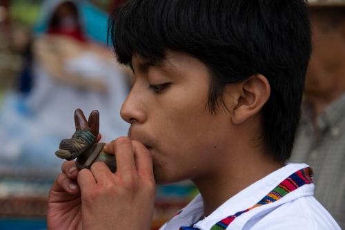 Close up of Kevin Cabrera Sánchez blowing into a traditional Guatemalan whistle during the ceremony of the first alfombra.