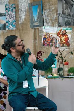 A man, seated, holds up an illustrated picture book, reading from it.