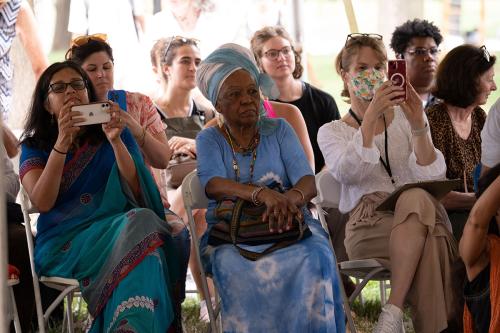 A crowd of seated people watch a performance, two holding up cellphones to record it.