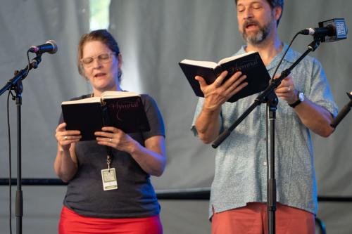Two people sing on stage, each holding hymnals.