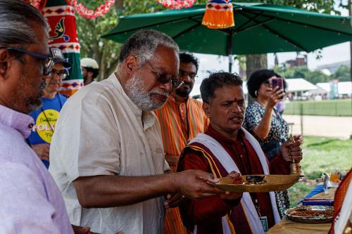 A man hands a tray to another by an atlar underneath a green umbrella.