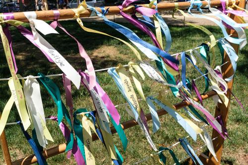 White, yellow, pink, blue, and green ribbons with different names written on fly in the wind, tied to a multi-layered structure of strings.