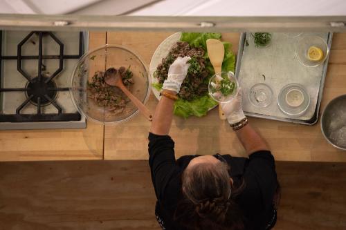 A photo of a mirror where a woman sprinkles cilantro over a plate of lettuce and sliced beef, all on top of a wooden table.