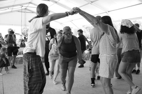 A woman ducks underneath the arms of two visitors raised above her head. The photo is shot in black and white.
