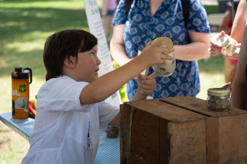A child points to a jar full of a white liquid with plants floating inside.