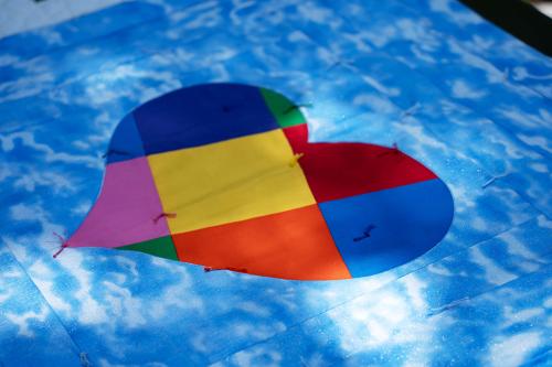 A quilt with cloudy-blue-sky background and a heart in red, blue, green, orange, and pink color blocks.